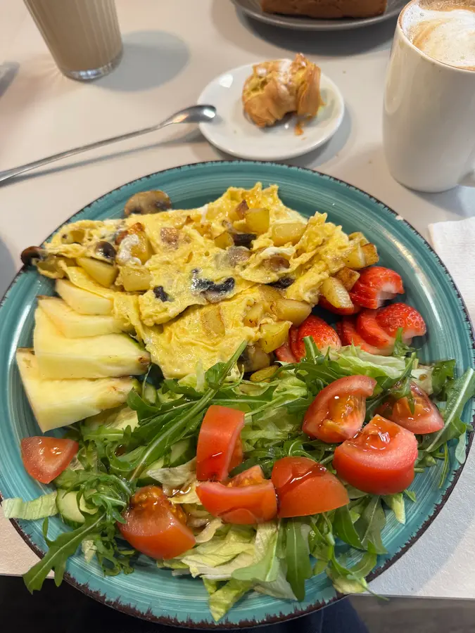 Omelett mit Champignons und Bratkartoffeln, Salat, Tomaten, Erdbeeren und Ananas auf türkisem Teller
