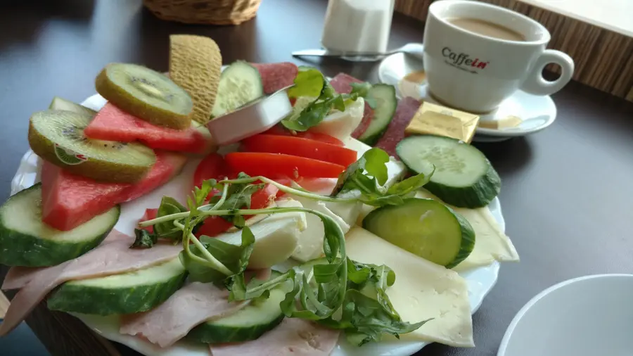 Frühstücksteller mit Käse, Aufschnitt, Gurke, Tomate, Kiwi und Melone, daneben ein Kaffee