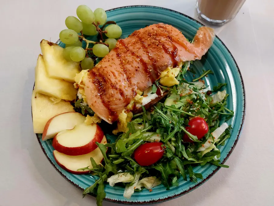 Lachs auf Brot mit Rührei, Rucola und Kirschtomaten, dazu Ananas, Apfel und Trauben